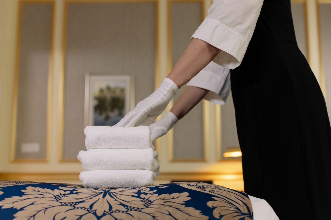 why-choose-us A hotel housekeeper neatly stacks fresh towels in a luxurious room setting.